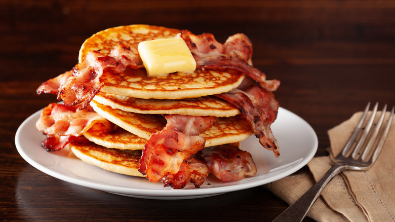 A stack of pancakes with strips of bacon and melting butter on it.