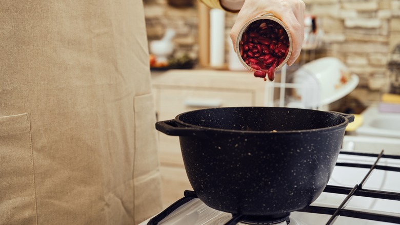 Person pouring can of beans into pot on stove