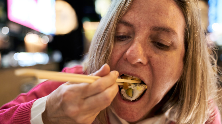 Person puts sushi in mouth with chopsticks