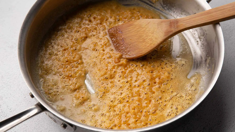 orangish-brown paste in a metal frying pan with a wooden spoon