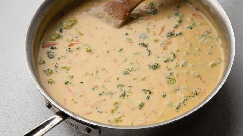 broccoli cheese soup in a metal frying pan with a wooden spoon