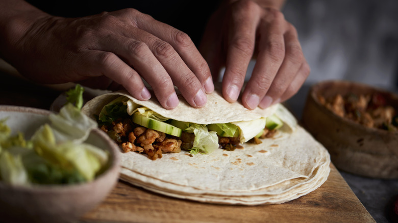 A chef folds a flour tortilla to make a bean burrito