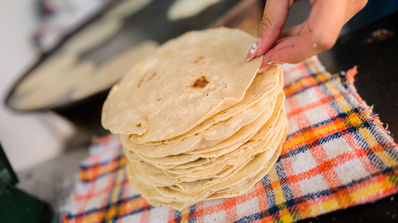 A woman picks a fresh tortilla off a tall stack