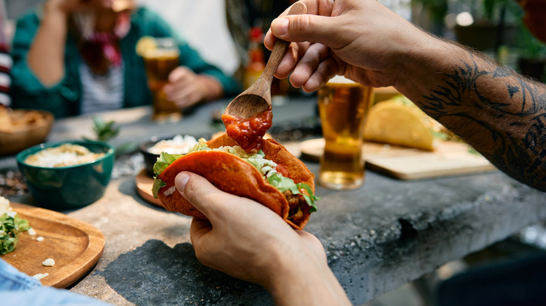 Man spoons salsa onto his loaded taco at a table with friends