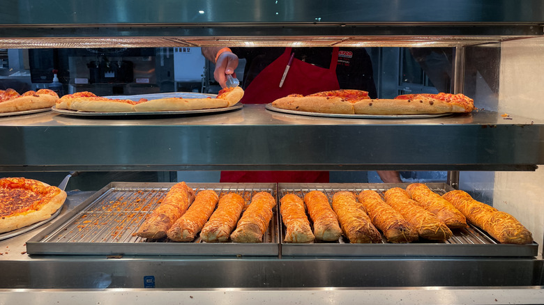 A Costco food court employee reaches for a slice of pizza on a warming tray