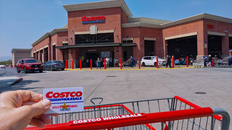 Hand holding Costco membership card in front of the store