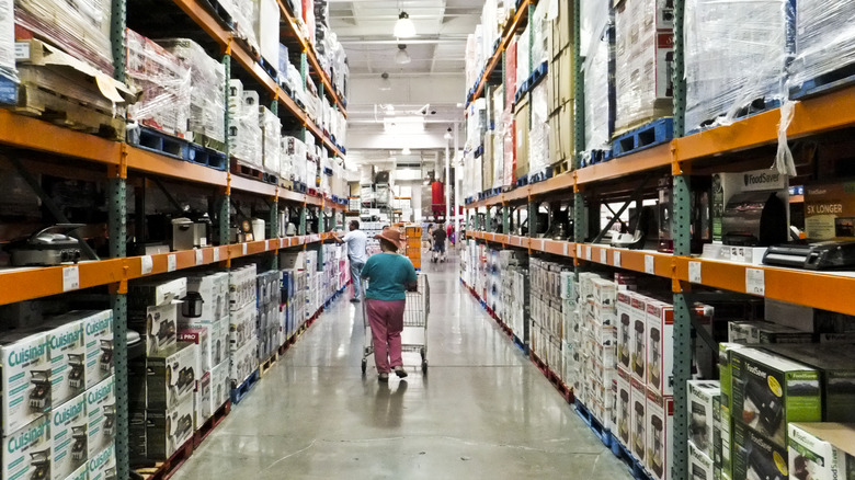 Customer walking down Costco aisle with shopping cart