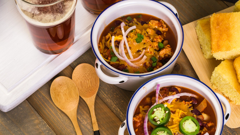 Two bowls of chili next to a pint glass of beer and cornbread