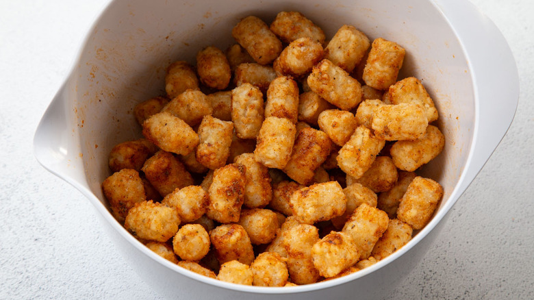 tater tots tossed wtih seasoned oil in bowl