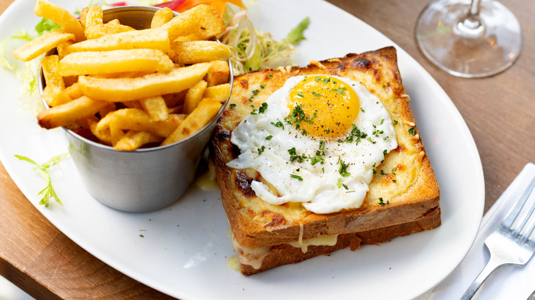 Croque madame sandwich on white plate with fries