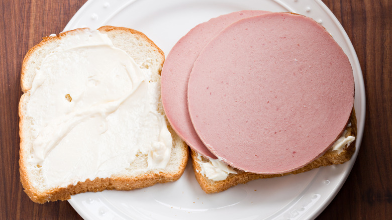 Slices of bologna on white bread with mayo on white plate