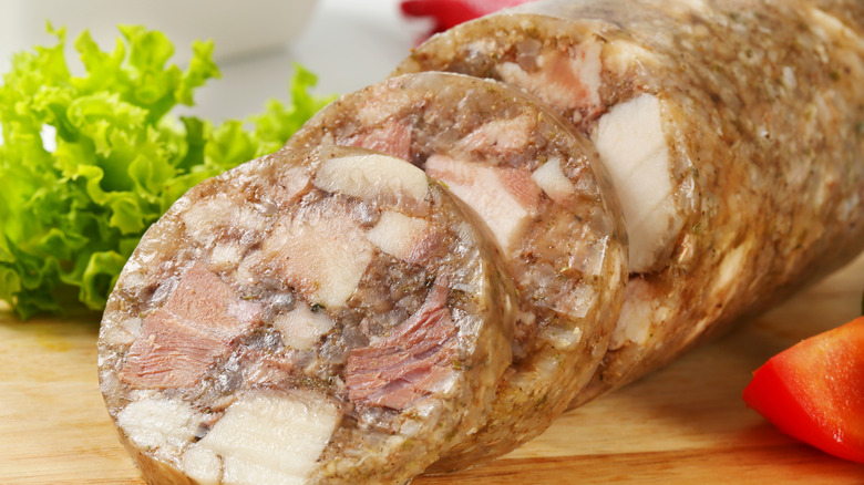 Sliced log of head cheese on wooden board with lettuce