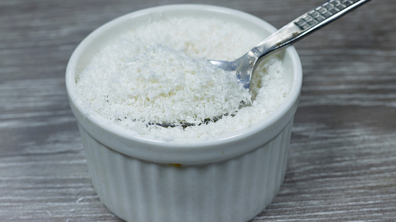 Desiccated coconut in a white bowl with a spoon on wooden table