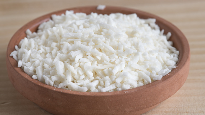 Shredded coconut in clay bowl on wooden surface.