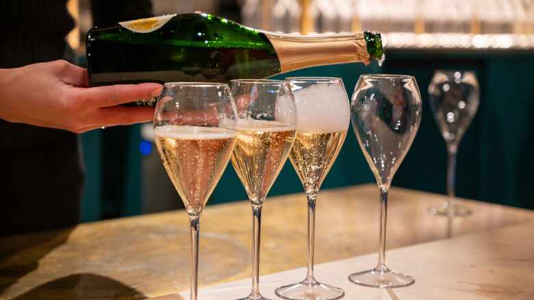 A person pouring a bottle of sparkling wine into four wine glasses.