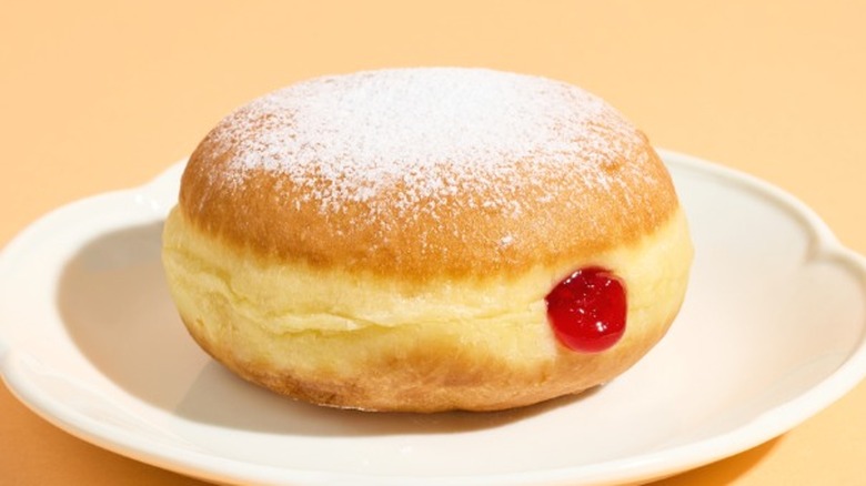 A jelly donut, dusted with powdered sugar, on a white plate.