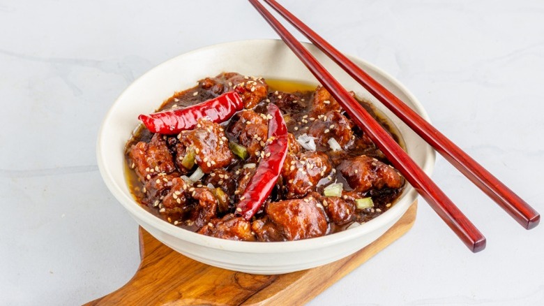 A bowl of General Tso's chicken with red chilis and chopsticks.