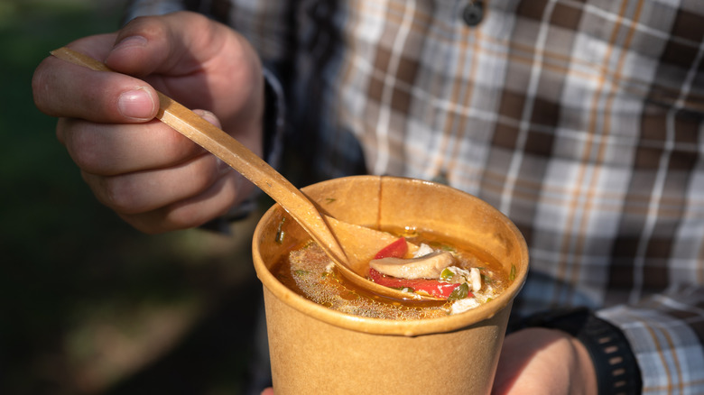 Hand with spoon in takeout soup tub