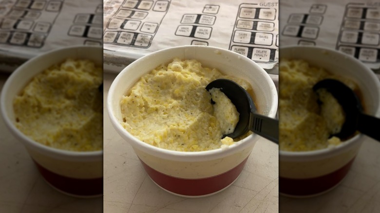 Black plastic spoon in tub of cheesy grits