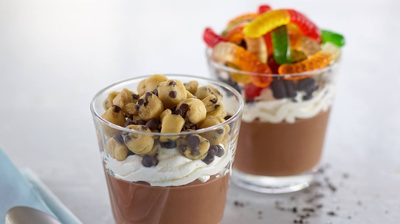 Two cups with chocolate pudding, cream, and cookie dough or gummy worms