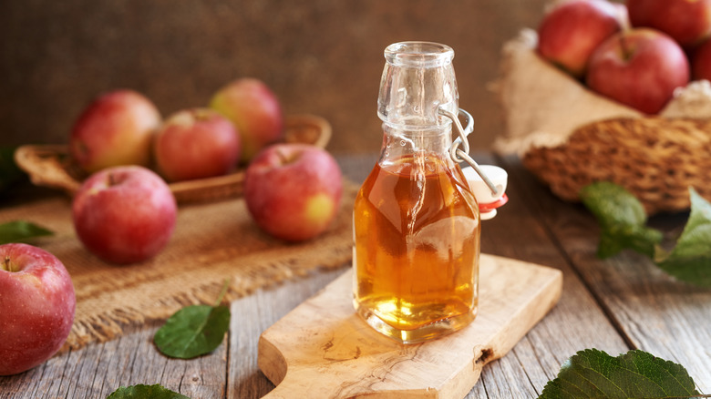 A glass container of apple cider on a wooden cutting board