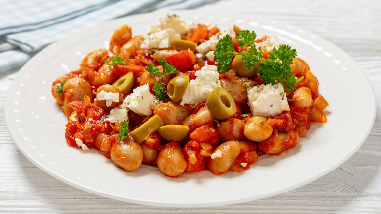 Plate of butter beans with tomato sauce, chopped olives, feta cheese, and parsley