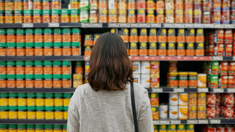 woman facing shelved canned goods