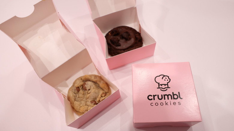 Three individual crumbl cookie boxes, two of which are open and displaying the cookies inside