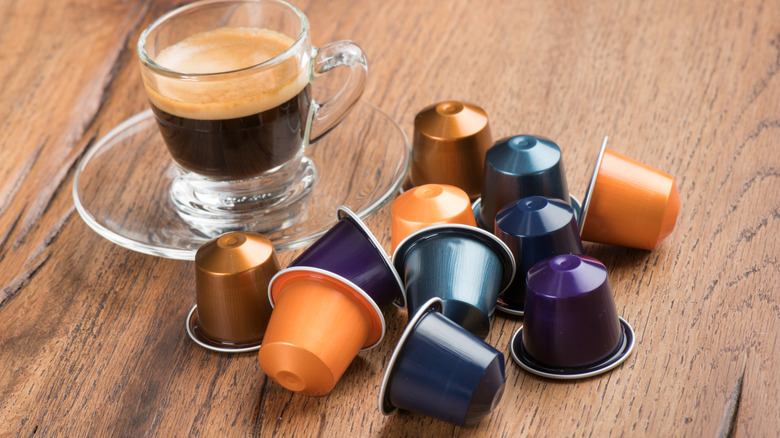 shot of espresso in a glass teacup beside multi-flavored Nespresso pods