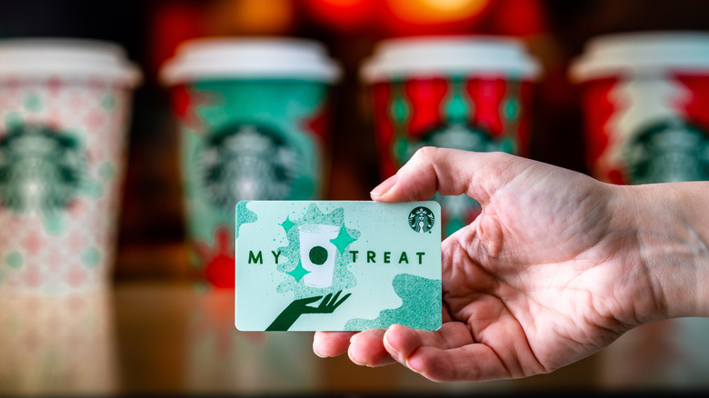 Starbucks gift card being held up with holiday to-go cups in the background