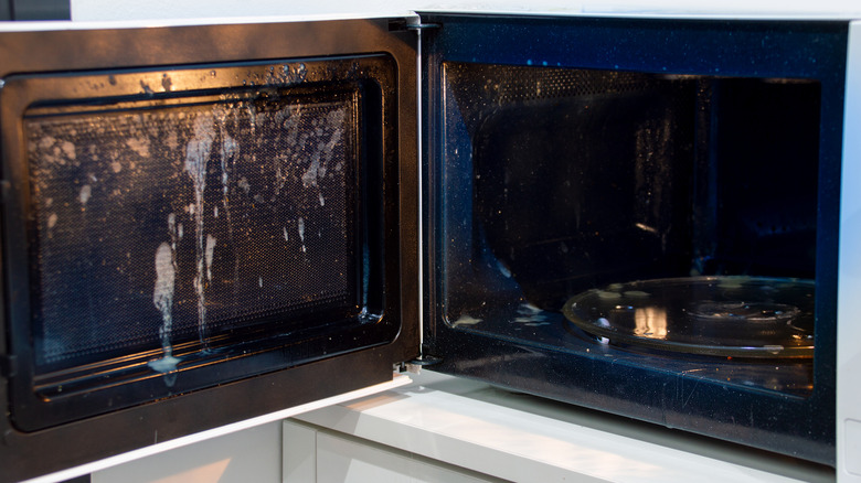 An open microwave revealing food splatter on the door and interior