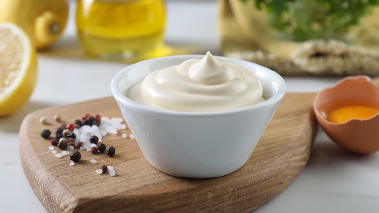 Mayonnaise bowl on wooden board with lemon, salt and pepper, oil, egg