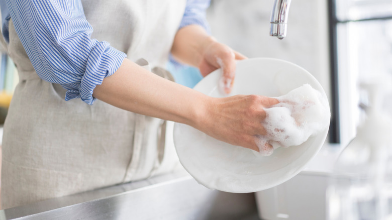 A woman using soap and water to wash a white plate