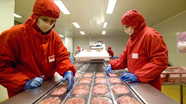 Factory workers inspect sliced salami on a production line