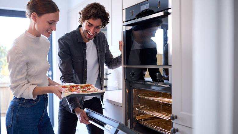 A couple placing a pizza into the oven