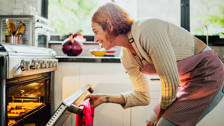 A woman opening an oven to check a batch of cookies