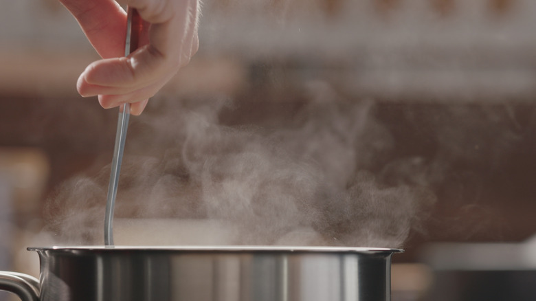 a hand holding a utensil and stirring a a pot on the stove