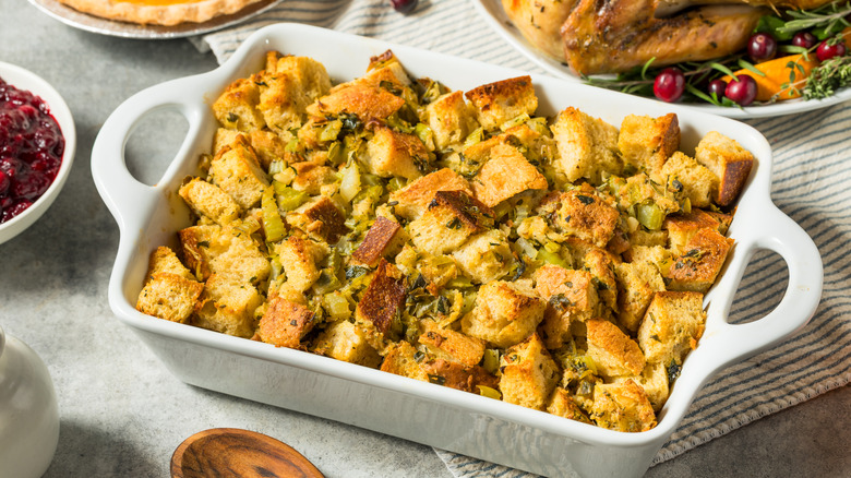 A white tray of Thanksgiving stuffing next to other plates of food.