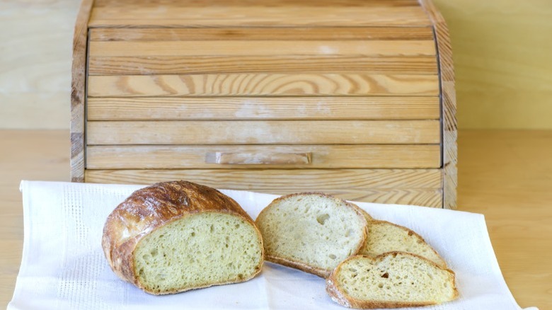 Homemade bread resting on white cloth in front of a closed wooden breadbox