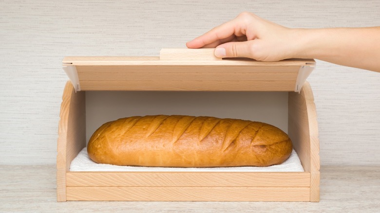 A loaf of bread inside an open wooden breadbox