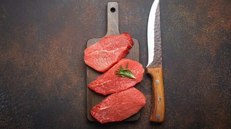 Three pieces of raw steak next to a large steak knife