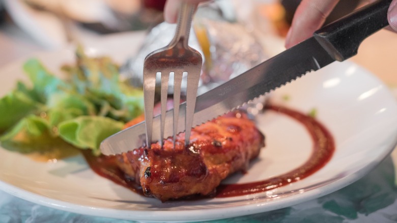 A diner cutting into a piece of meat with a fork and serrated steak knife