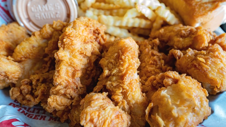 A basket of Raising Cane's chicken fingers and fries, with a container of Cane's Sauce in the background.