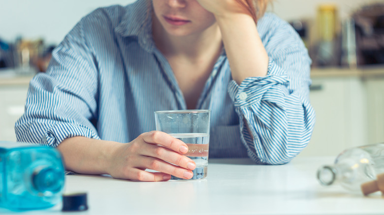 Person holding a glass of water surrounded by empty alcohol bottles