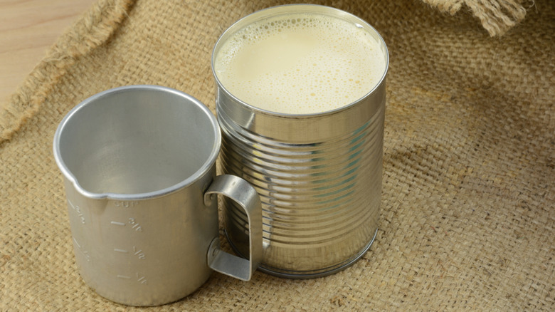 Open can of evaporated milk with tin cup