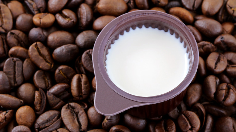 Close up of a small open container of coffee creamer on top of coffee beans