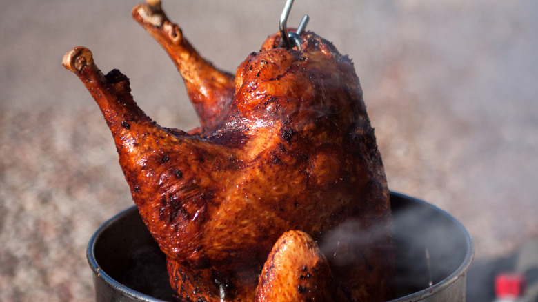 A deep-fried turkey is pulled from the frying tank on a metal hook