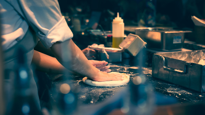 hands preparing pizza dough on restaurant station