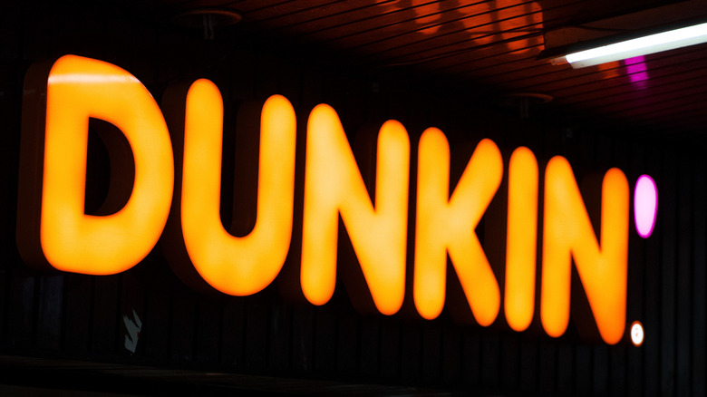 A neon sign that reads DUNKIN' glowing in the dark