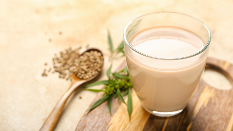 glass of creamy hemp milk beside wooden spoon of hemp seeds over wooden background